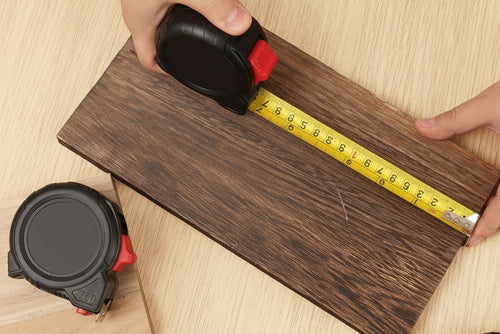 Person measuring wooden planks with a tape measure on a wooden surface